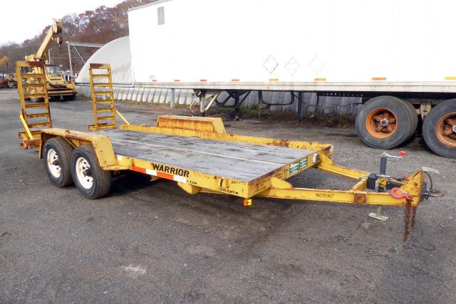 Yellow Warrior tilt-bed trailer with dual axles and loading ramps showing structural steel deck and hitch.