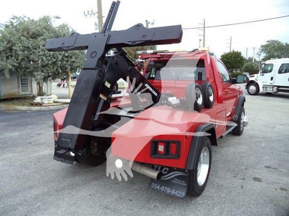 Tow truck with a large black hitch/boom hoist attached to a red Ram 4500 chassis; rear view shows dual rear wheels and hitch mechanism.