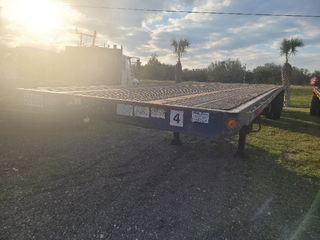 Flatbed trailer in an open lot showing rear end; 2009 Great Dane 48x102 trailer with mesh deck, blue frame, numbered stickers, and rear left and right support legs.