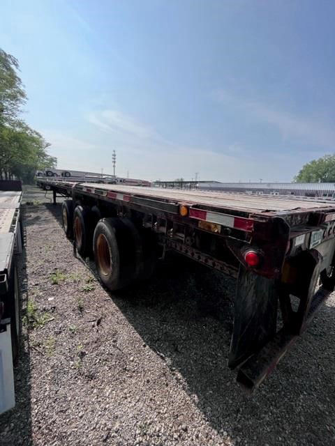 Flatbed trailer view showing long steel deck with dual rear axles and mud flaps.