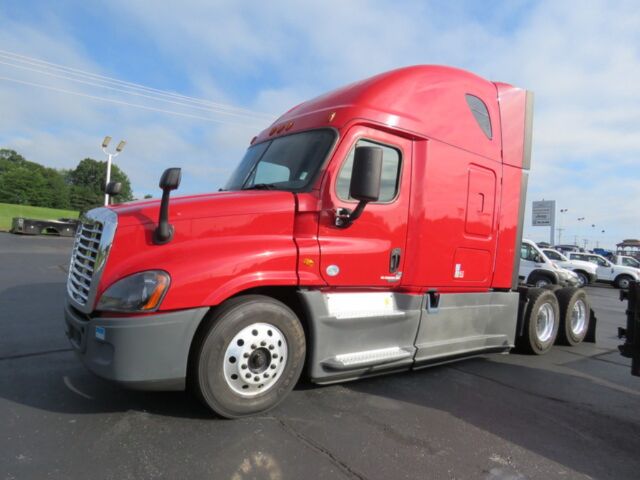 Red Freightliner Cascadia Evolution semi-truck tractor front-left view, sleeper cab, black wheels, gray lower body panels, blue sky.
