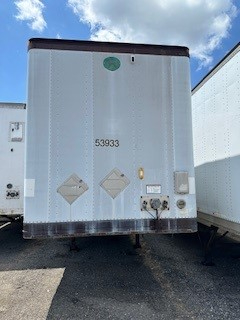 Rear view of a light gray 2001 Great Dane dry van trailer with two diamond hazard placards, a small circular green sticker near top, and the number 53933 on the door area.
