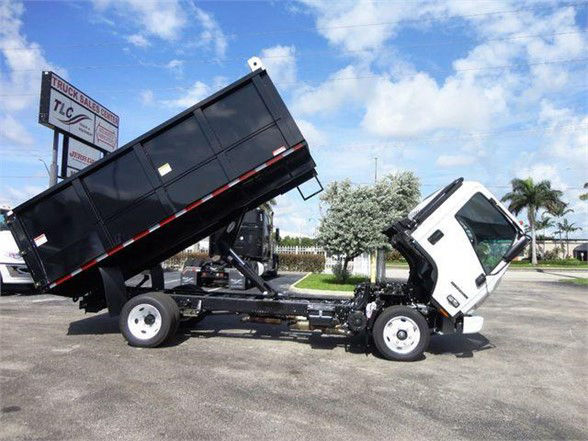 Isuzu NPR HD dump truck with tilt bed raised, black dump body, white cab, on a lot.