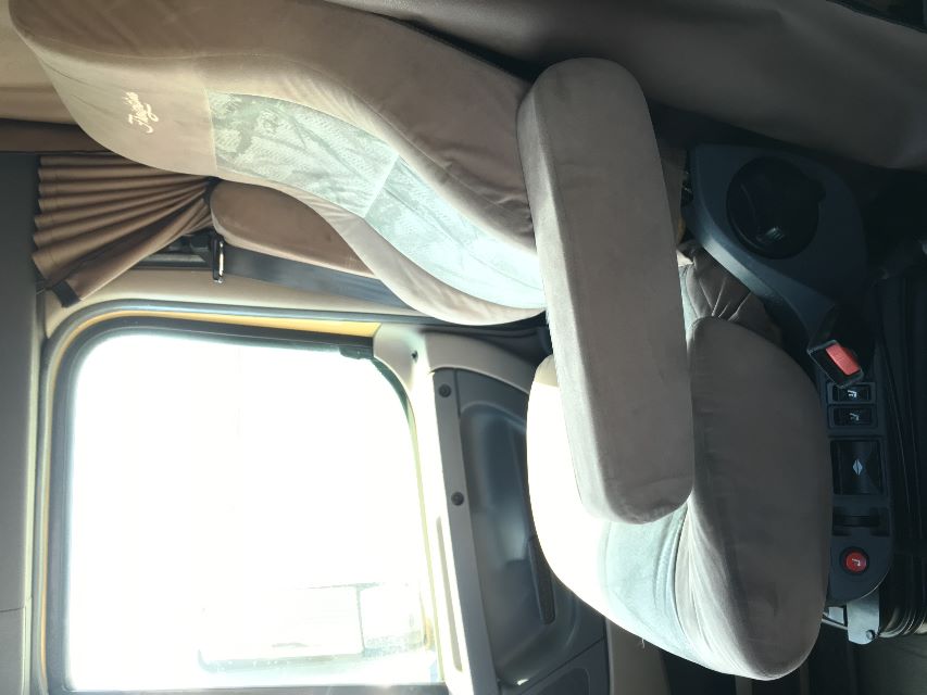 Cab interior of a Freightliner Cascadia 125 truck cab showing the driver seat with armrest, window, and control switches at the base.
