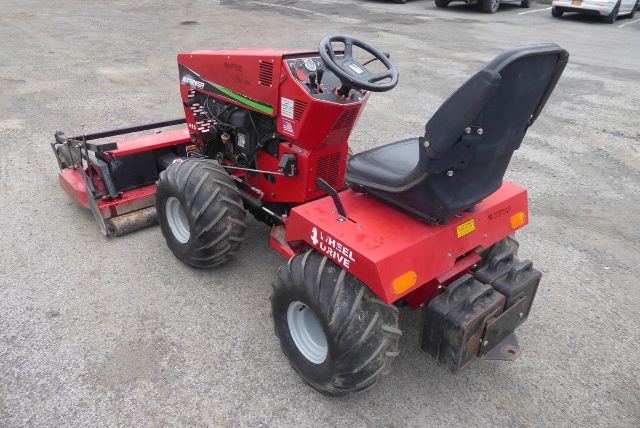 Steiner 415 utility tractor with red body, black seat, steering wheel, and rear turf tires; attached front mower deck and rear weight blocks.