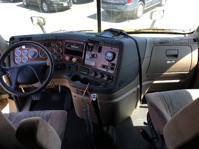 Truck interior cab of a 2010 Freightliner Cascadia 125 showing dashboard with gauges, steering wheel, gear shifter, and driver seat.