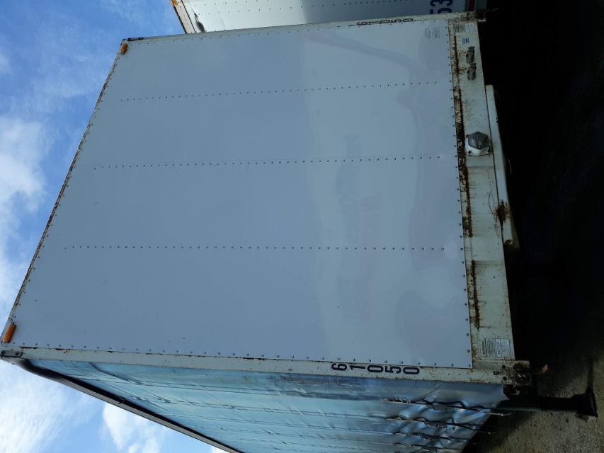 Trailer rear door on a light blue utility truck trailer with riveted panels and rust along the lower edge, showing wheel cutout and step area.