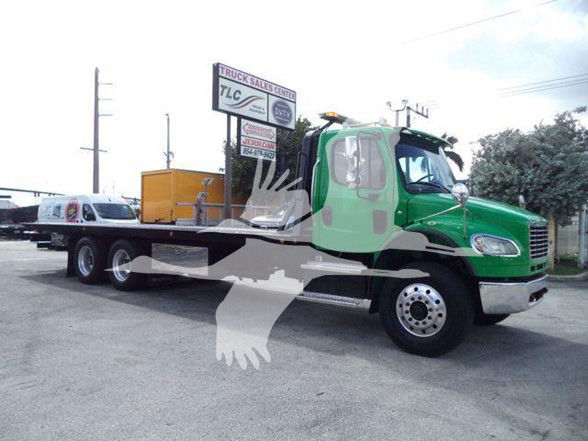 Freightliner BUSINESS CLASS M2 106 tow truck side view showing green cab and flatbed.