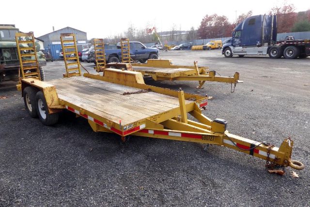 Trailer with dual-axle flatbed car hauler showing wooden deck and metal ramps in yard.