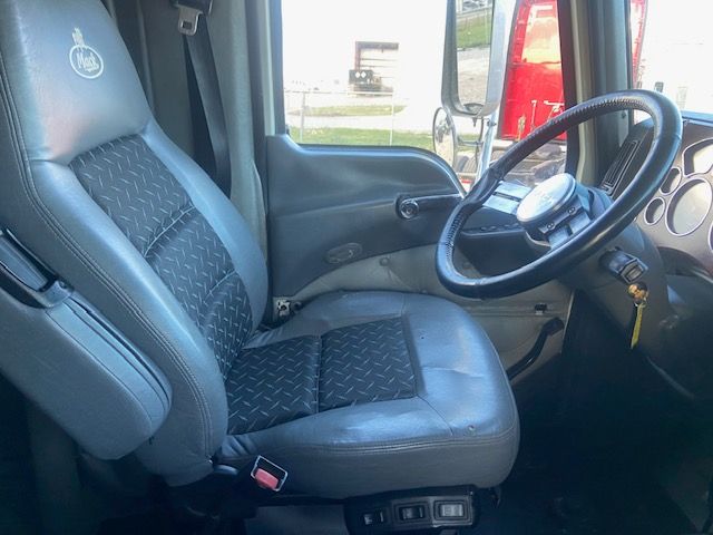 Truck cabin interior with driver's seat, steering wheel, and dashboard. Visible text includes Mack logo on seat headrest. No engine or model badges readable inside.