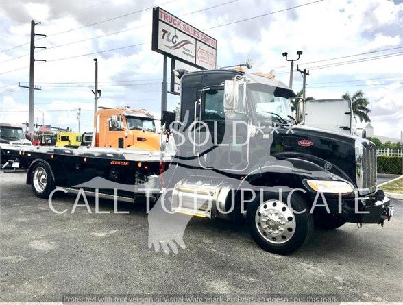 Peterbilt 337 tow truck in black with chrome accents, flatbed trailer attached, showroom sign in background.