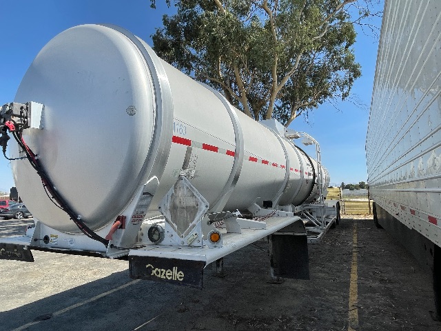 2011 Heil 407 crude oil trailer with cylindrical aluminum tank and rear landing gear, parked between two trailers in a lot.
