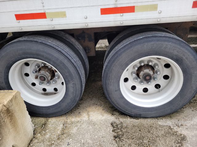 Two rear trailer axles with dual wheels, white rims, black tires, undercarriage and frame visible. No legible labels visible on tires or hub areas.