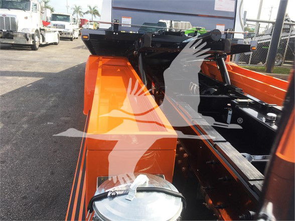 Front view of a 2022 Peterbilt 337 chassis with bright orange components and frame, showing equipment mounting areas and part of the cab behind.