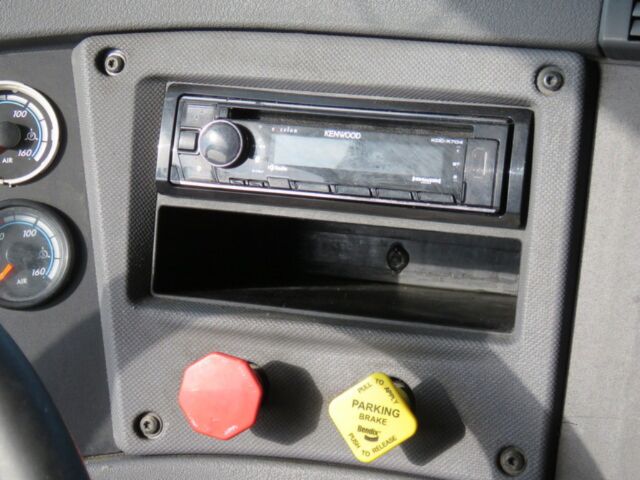 Truck dash area showing Kenwood stereo head unit, storage pocket, red push knob, and yellow parking brake knob.