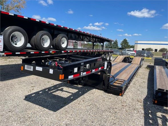 Fontaine 55 ton steel roller paver lowboy trailer showing 24 ft deck with black frame and dual axles, storage toolbox, and ramps, outdoor lot.