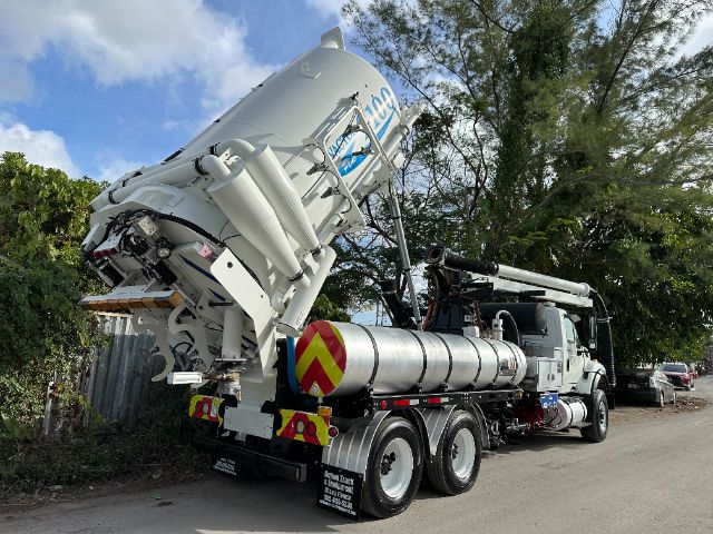 Vacuum truck chassis with large rear tank and mounted booster unit, International 7500 badge visible, rear wheels in dual configuration, equipment piping and hoses present.