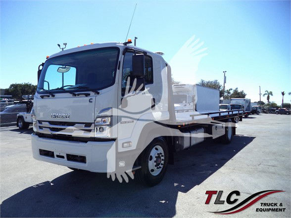 Isuzu FTR tow truck in a dealership lot with a flatbed body, white cab, and TLC Truck & Equipment watermark.