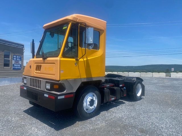 Ottawa T2 truck cab in yellow and tan, front-left view in a lot with gravel surface and clear blue sky.
