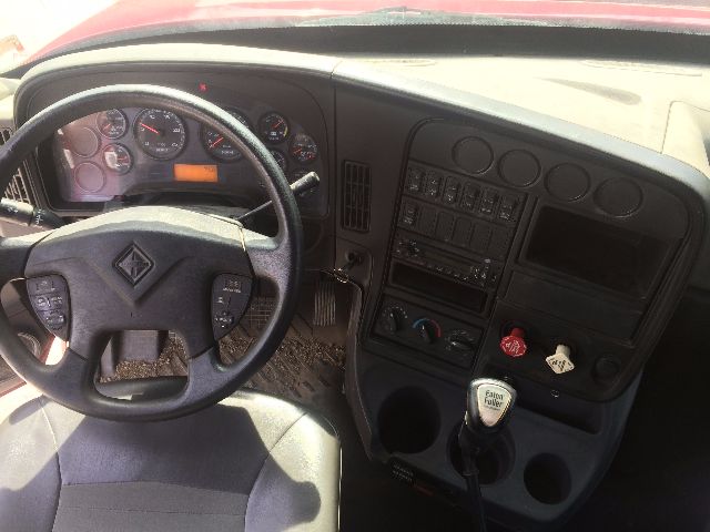  cab interior of a 2011 International Prostar showing steering wheel, dashboard gauges, manual shifter, and center console with switches.