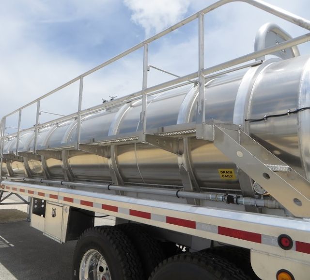 Aluminum vacuum tanker trailer with side ladder and polished cylindrical tank. Visible labels include 'DRAIN DAILY' on a small yellow tag near the frame.