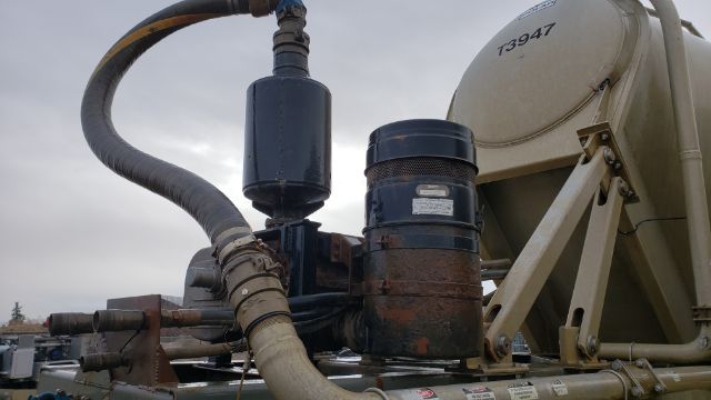 Tubing and hoses connected to a tank trailer with a large cylindrical component and cylindrical filter, T93947 identifier on tan tank.