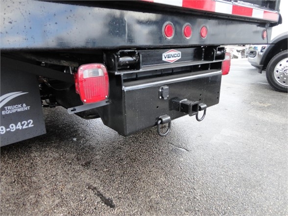Ram 3500 dump truck rear with black metal toolbox and hitch mounts under tailgate; visible red taillight, VenCo logo plate on hitch, trailer hitch rings, and dump bed underside.