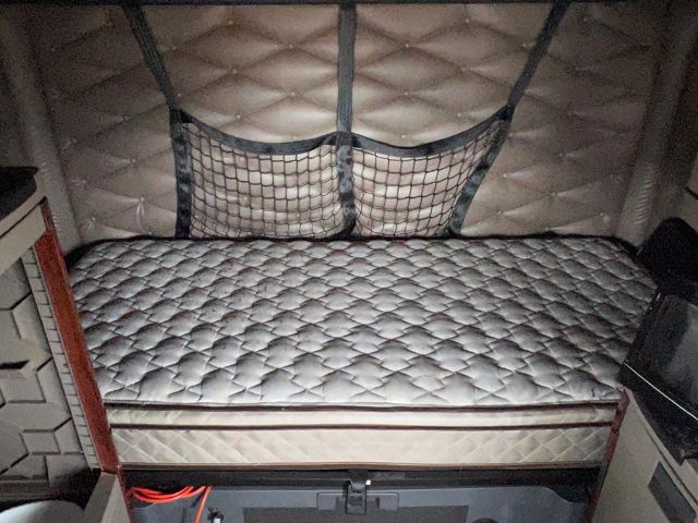 Truck sleeper cab interior with quilted bed mattress and storage pockets, part of a Freightliner Cascadia sleeper cab.