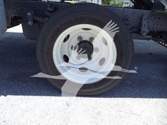 Truck wheel close-up showing white steel rim and black tire; part of truck frame visible above; no legible labels seen.