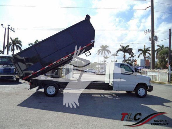 Ford E450 dump truck with raised dump bed in a dealership lot.