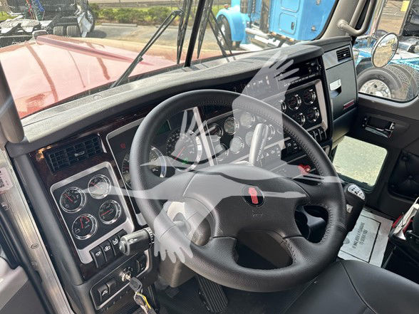 Kenworth W900L truck interior cockpit with steering wheel and dashboard gauges visible through driver's window.