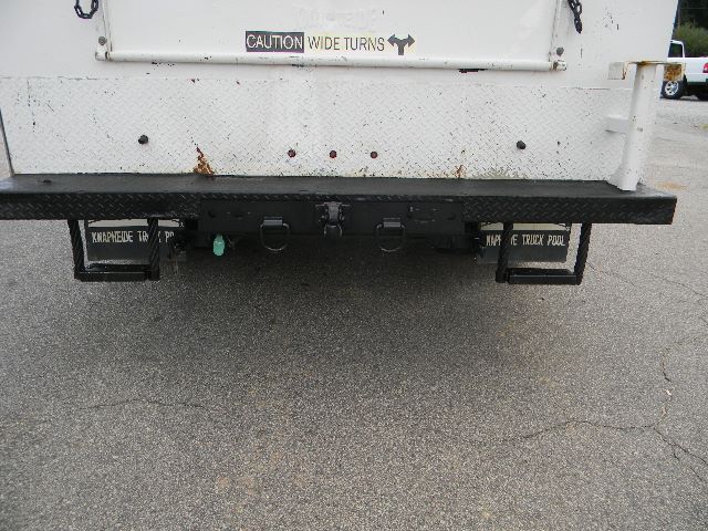 Rear view of a 2011 Ford F-750 Super Duty Crew Cab service truck showing a flatbed with hooks, lights, and a caution label 'CAUTION WIDE TURNS' on the tailgate.