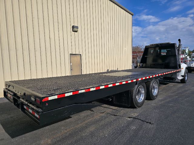 Peterbilt 348 rollback tow truck with long flatbed and dual rear axles, viewed from rear-left side.