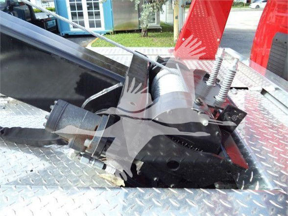 Tow hitch or heavy-duty truck component on diamond-plate surface with hydraulic/metal hardware, bolts, and springs; faint watermark of a bird in flight over the center.