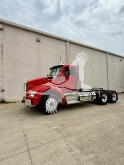 Kenworth T880 conventional day cab truck in red with chrome exhaust stacks and dual rear axles, front view at an outdoor lot.