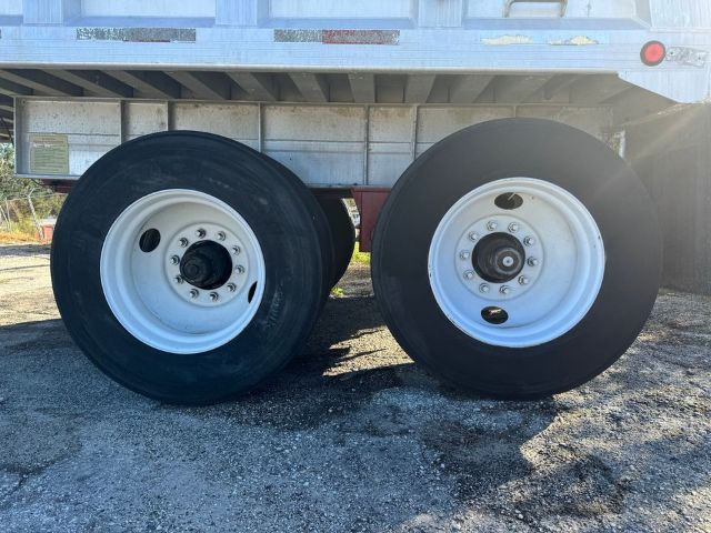 Two rear wheels of a dump trailer with white rims and black tires under a frameless GMC unit.