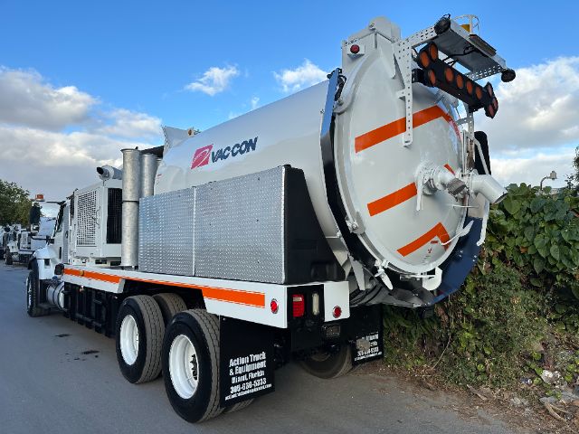 Vacuum truck rear with large circular vacuum hopper and orange safety stripes, Vac-Con branding on side, rear lights, and heavy-duty tires.