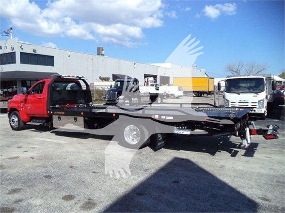 2023 Chevrolet Silverado 6500HD tow truck with flatbed trailer in front of a dealership lot.