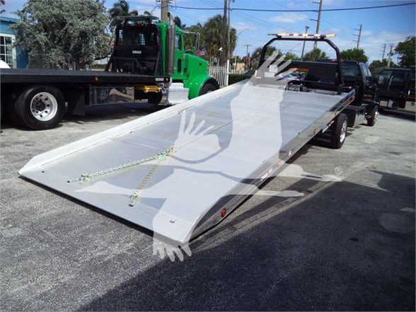 Flatbed tow truck trailer with metal ramp and straps, license plate not visible.