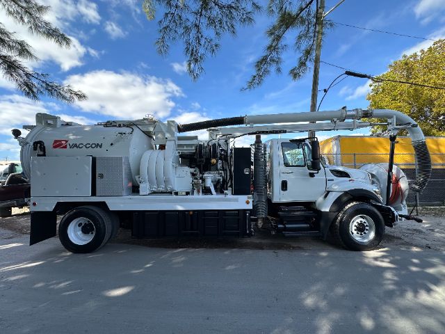 Vacuum truck with Vac-Con logo showing large cylindrical waste tank and hose reel, side compartments, and exhaust piping.