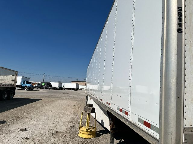 Trailer side of a white Great Dane Champion trailer with a blue sky, showing riveted panels and rear wheels.