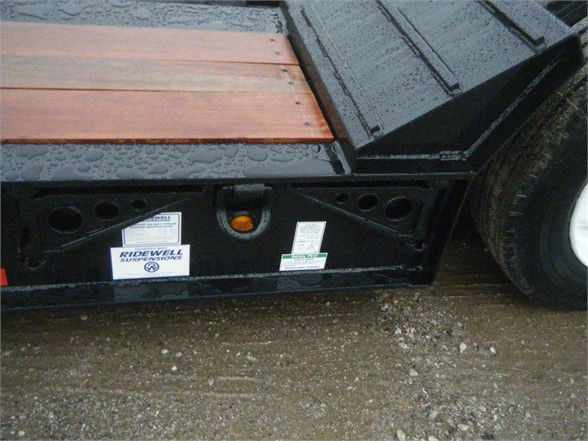 Lowboy trailer deck with wooden planks and Sidewell suspensions sticker showing QA labels and warning placards.