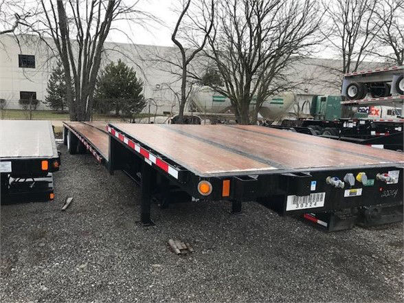 Flatbed trailer on a gravel lot with a wooden deck, rear view showing connectors and lights.