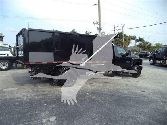 Vehicle side view: 2023 Chevrolet Silverado 6500HD dump truck with black cab and dump bed in a lot. Visible text not legible due to distance.