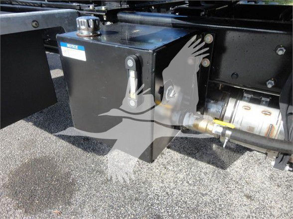 Boxed component attached to truck frame with label 'WORKS' and a hose fitting; diesel/engine area with mechanical linkage and hydraulic lines.