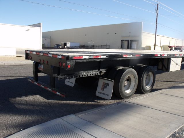 Flatbed trailer with expandable sections and dual rear axles, black frame, Onan? No visible branding. Side clearance lights and reflectors along the rails.