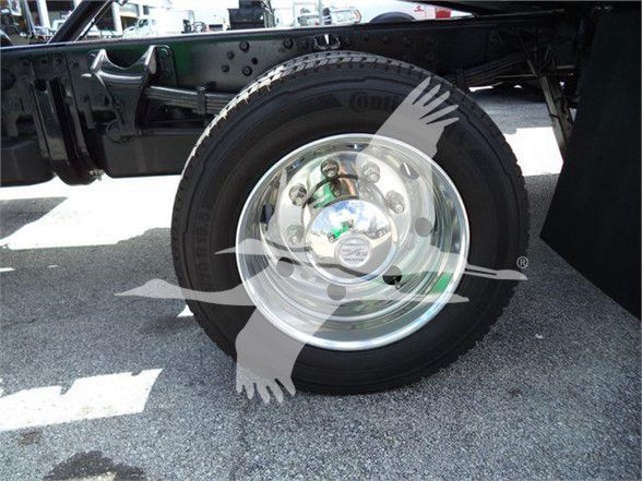 Wheel and tire assembly on a truck chassis showing chrome hubcap and tire with visible lug nuts.