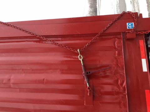 Trailer side with red container and chain links securing latch, visible hinge and chain attached to door