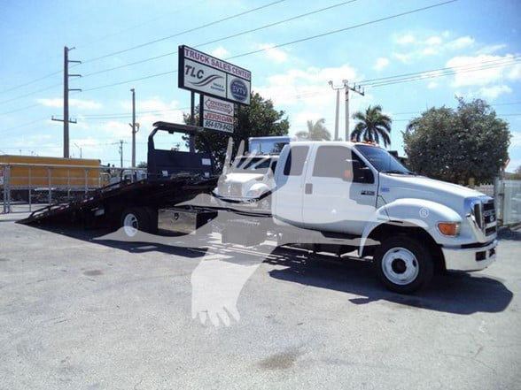 2015 Ford F650 XLT tow truck with flatbed, white cab, long dual rear wheels, dealership lot in background