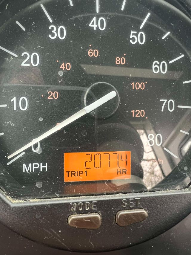 Dashboard of a vehicle showing speedometer with large numbers, orange digital trip display reading 'TRIP1 HR 2077.4', and MODE/SET buttons at bottom.